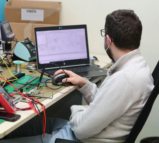 Photo d'une personne travaillant devant un ordinateur avec un circuit électronique posé sur la table