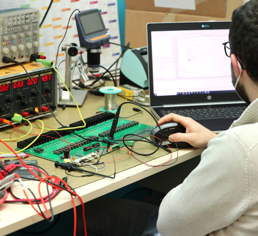 Photo d'une personne travaillant devant un ordinateur avec un circuit électronique posé sur la table