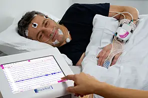Photo montrant un patient dans un lit d'hôpital à droite pour des tests d'apnée du sommeilt avec l'interface de mesure au 1er plan en bas à gauche