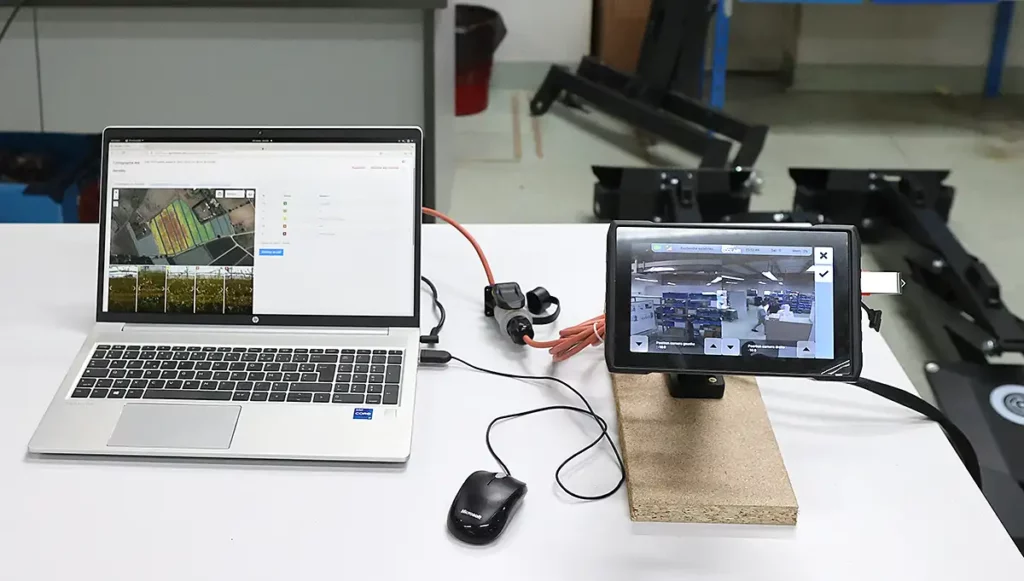 Photo montrant un PC de développement à gauche, posée sur une table, et une interface tactile IHM à droite sur un socle en bois